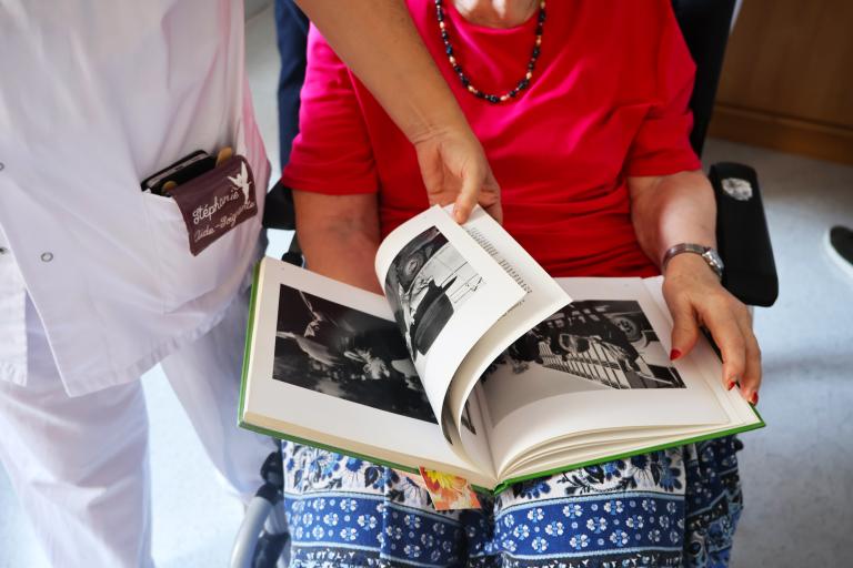 Une patiente d'EHPAD feuillette, avec une soignante, un livre offert par la Médiathèque départementale du Puy-de-Dôme
